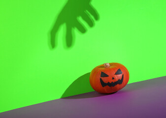 Halloween pumpkin with hand shadow on green purple background. Creative halloween layout. Minimal still life