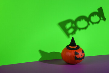Halloween pumpkin with boo! word shadow on green purple background. Creative halloween layout. Minimal still life