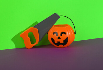 Halloween bucket pumpkin for candy with saw on green purple background. Trick or Treat