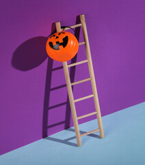 Wooden ladder with Halloween candy bucket on a purple background. Minimal halloween layout.