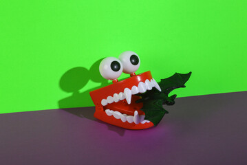 Halloween still life. Monster clockwork jaw with bat on green purple background