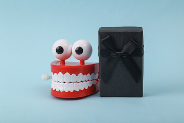 Funny toy clockwork jumping teeth with eyes and gift box on blue background.