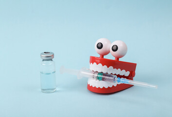 Funny toy clockwork jumping teeth with eyes holding syringe on blue background. Vaccination