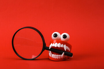 Funny toy clockwork jumping monster teeth with eyes holding magnifying glass on red background.