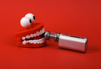 Funny toy clockwork jumping teeth with vaping device on red background.