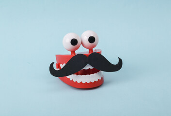 Funny toy clockwork jumping teeth with eyes and mustache on blue background.