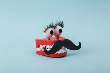 Funny toy clockwork jumping teeth with eyes and false eyelashes, mustache on blue background....