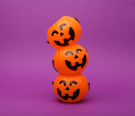 Stack of halloween pumpkins orange candy buckets with face on purple background. Trick or Treat