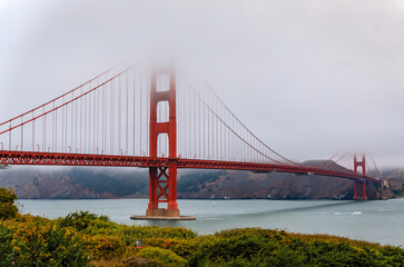 The famous Golden Gate bridge on a cloudy summer day with low hanging fog rolling in San Francisco,...