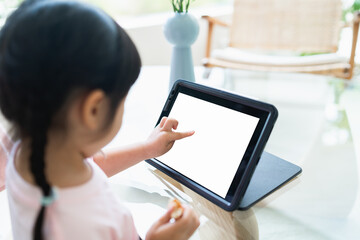 Asian girl looking and touch on white screen at the tablet screen attentively. overstimulated children concept. Too much screen time. asian girl watching videos while tv is working.