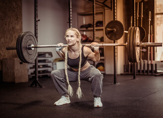 Fototapeta na wymiar Young fit woman doing squats with heavy barbell on her shoulders in modern gym. Functional, training muscles legs and buttocks