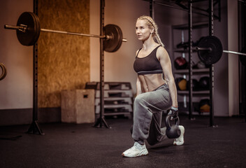 Fit woman in sportswear doing lunges with a kettlebells in her hands in gym. Functional training