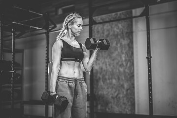 Muscular attractive woman training biceps with dumbbells in her hands, functional gym, weights training.