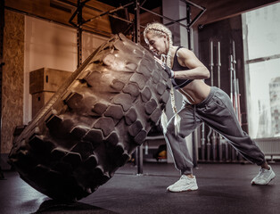 Obraz na płótnie Canvas Fit female athlete flipping huge tire. Woman lifts a heavy wheel. Muscular young woman doing functional training exercise at gym.