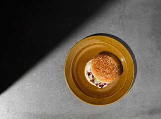 American burger with beef, camambert cheese and jam on plate on gray concrete table. Beef burger with hard shadow and dark stone background. Homemade burger in dark style. Fastfood menu. Junk food.