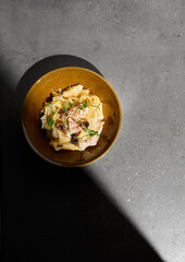 Italian pasta Pappardelle with chicken and mushrooms in creamy sauce on gray stone table. Creamy pasta pappardelle with chicken meat and mushroom. Fettucine fungi on concrete background with shadow.