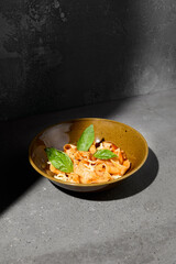 Italian pasta Pappardelle with tomato and mozzarella cheese on gray stone table. Tomato pasta pappardelle with cheese and basil. Veggie pasta with tomatoes on concrete background and shadow.