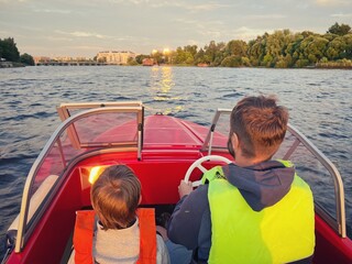 Father and son riding motor boat wearing safety vests having a ride in Neva river, Saint Petersburg