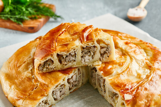 Classic turkish pie with meat on wooden board. Composition with burek pie on concrete background with textile and spices. Balkan pie with minced meat  in rustic style on gray table.