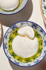 Aesthetic composition with burrata cheese and mozzarella in olive oil. Fresh burrata and mozzarella cheese in ceramic bowl. Italian cuisine. Dairy cheese: mozzarella buffalo and creamy burrata.