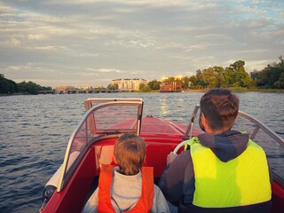 Father and son riding motor boat wearing safety vests having a ride in Neva river, Saint Petersburg