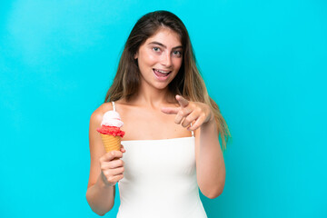 Young woman in swimsuit holding an ice cream isolated on blue background points finger at you with a confident expression