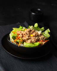Close up of tuna salad bowl with lettuce, tomatoes and other vegetables on black background