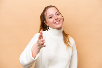 Young caucasian woman isolated on beige background shaking hands for closing a good deal