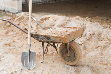 Construction cart with sand and shovel outdoors. Wheelbarrow for transporting goods at construction...