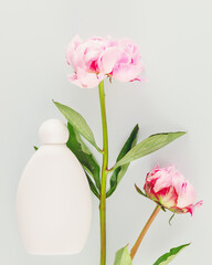 Mock up of natural, flower beauty product. White cosmetic bottle with two beautiful, pink peonies on a blue background. Minimalist composition with flowers and bottle with cosmetic product