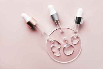 Three pipettes with different samples of gels cosmetic products in petri dish on pink background