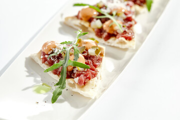 Beef tartare on crispy focaccia isolated on white background. Appetizer from minced meat with spicy sauce on toast.  Starter food meat tartare in French style. Contemporary food for restaurant.