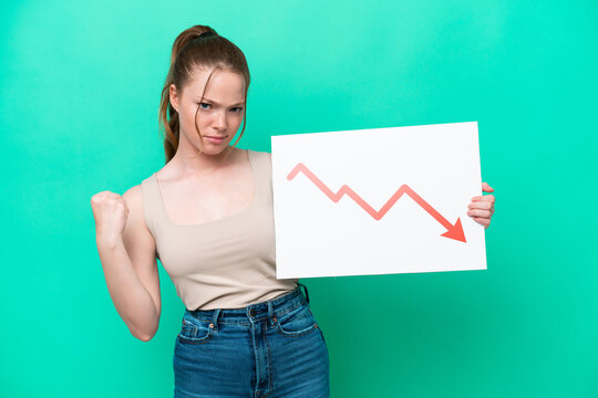 Young caucasian woman isolated on green background holding a sign with a decreasing statistics arrow symbol and angry