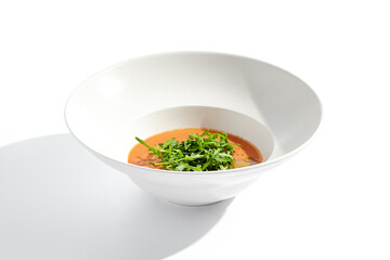 Summer Spanish soup - gazpacho with rocket salad isolated on white background. Vegetarian cold tomato soup in white plate. Meatless food in menu. Veggie lunch. Healthy food. Plant based eating.