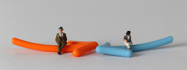 A miniature man and a miniature woman sitting on an arrow. Miniature people and business concept.
