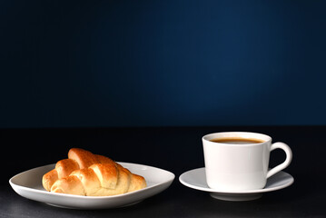 Croissant and coffee in white dishes on a dark background.