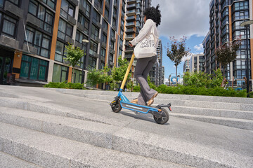 Woman rides around the city on an electric scooter with shopper on her shoulder