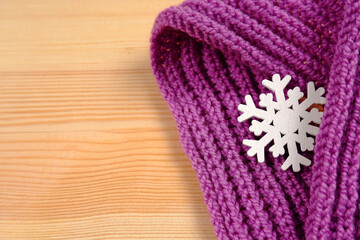 Obraz na płótnie Canvas A wooden white snowflake wrapped in a purple knitted scarf on a wooden background.The concept of warm winter clothes, natural blanks for creativity.Passion for knitting.Cold. Copyspace