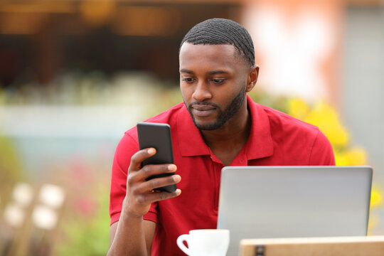 Black man in red using phone and laptop in a terrace
