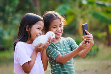 Two asian girls taking a picture and playing with adorable bunny. Sister siblings holding a little...