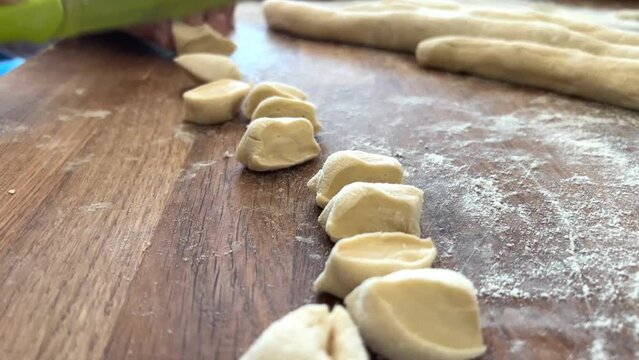 grandmother prepares delicious dumplings or pies or dumplings for her grandson she shakes dough, cuts it into pieces and sculpts on the table there are circles of dough she is sprinkled with flour
