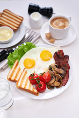 Fried eggs, bacon, tomato, toasted bread in white ceramic plate and cup of coffee