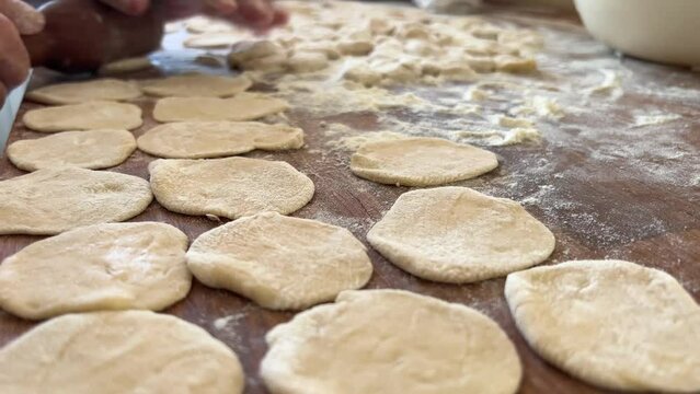 grandmother prepares delicious dumplings or pies or dumplings for her grandson she shakes dough, cuts it into pieces and sculpts on the table there are circles of dough she is sprinkled with flour
