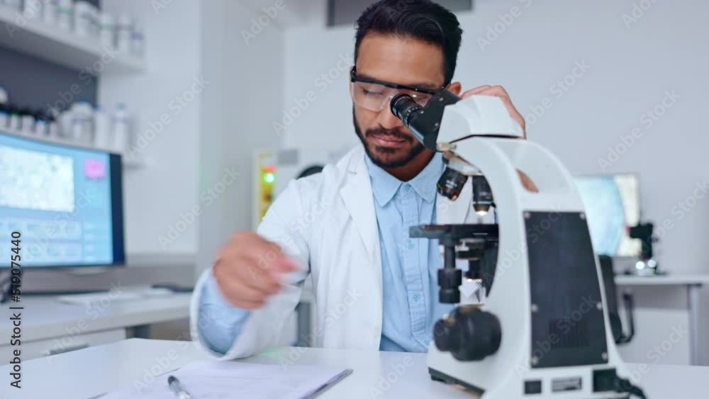 Poster male scientist using microscope looking at a blood sample and writing notes on his findings in a med
