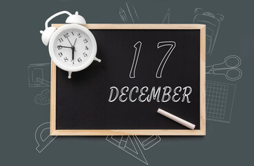 december 17. 17th day of month, calendar date. Blackboard with piece of chalk and white alarm clock on green background. Concept of day of year, time planner, winter month