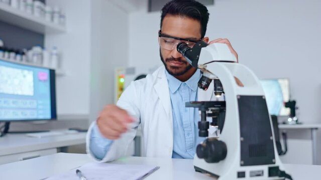Male scientist using microscope looking at a blood sample and writing notes on his findings in a medical research laboratory. Biotechnology specialist does analysis of dna with handheld camera motion