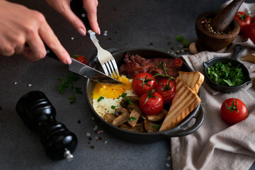 Fried eggs, bacon, tomato and toasted bread in a black ceramic pan at domestic kitchen