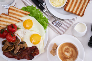 Fried eggs, bacon, tomato, toasted bread in white ceramic plate and cup of coffee