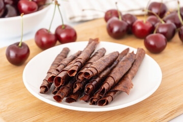 Red fruit leather rolls. Mashed sweet cherry snack. Homemade pastila on white plate on wooden board.