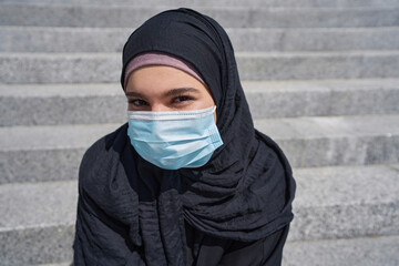 Woman in a hijab sits on the stairs wearing a mask